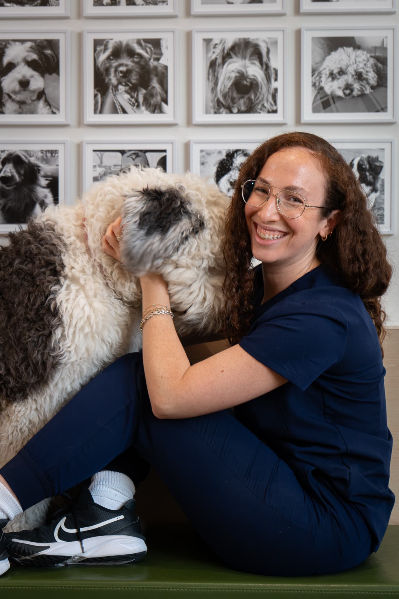 Upper Village team member sitting with a happy dog in front of the patient photo wall